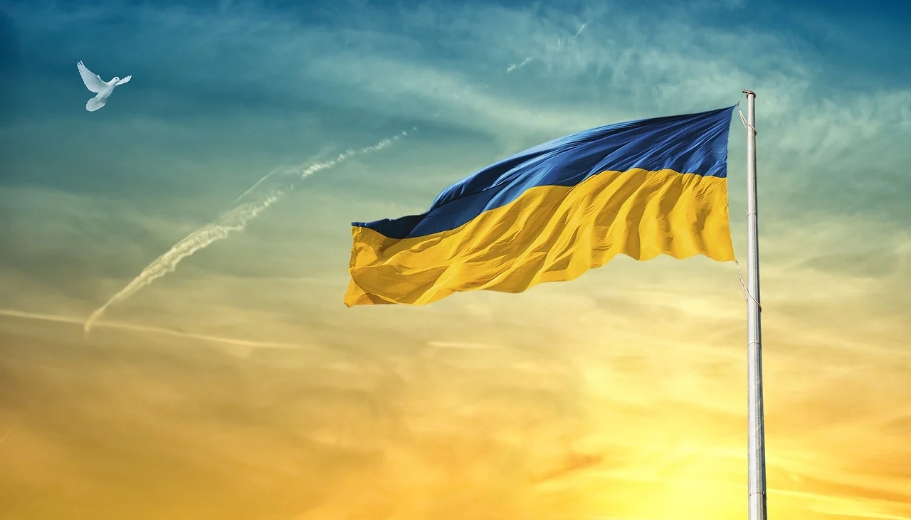 The blue-and-yellow flag of Ukraine against a golden sky, with a dove flying